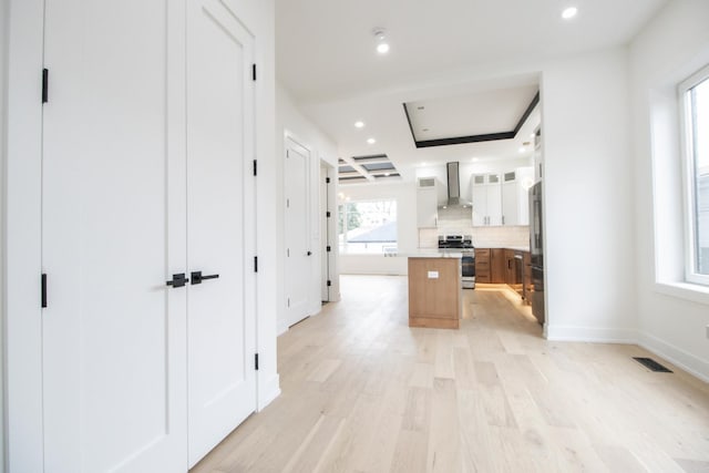 kitchen with a center island, wall chimney exhaust hood, light hardwood / wood-style flooring, decorative backsplash, and appliances with stainless steel finishes