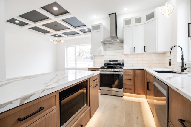 kitchen with appliances with stainless steel finishes, coffered ceiling, wall chimney exhaust hood, sink, and white cabinetry