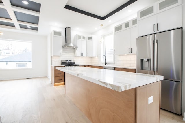 kitchen featuring a center island, wall chimney exhaust hood, a wealth of natural light, appliances with stainless steel finishes, and white cabinetry