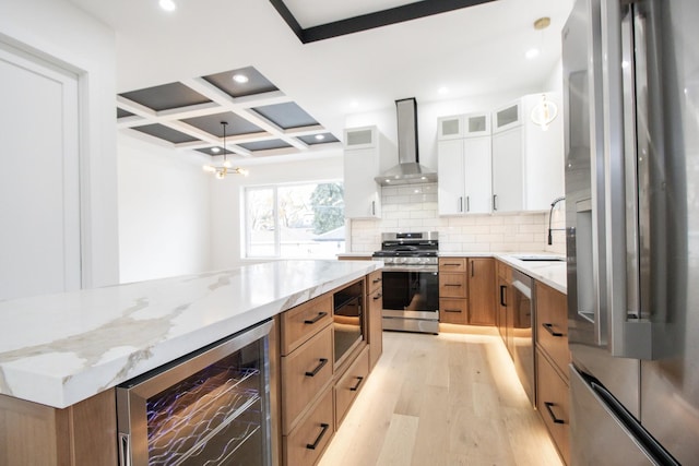 kitchen featuring stainless steel appliances, coffered ceiling, wall chimney range hood, wine cooler, and white cabinets