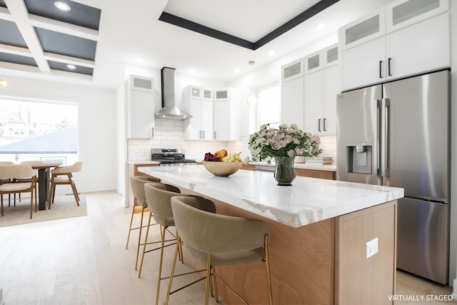 kitchen featuring wall chimney exhaust hood, stainless steel appliances, a kitchen island, light hardwood / wood-style floors, and white cabinetry