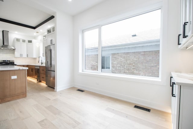 kitchen with light wood-type flooring, stainless steel appliances, sink, wall chimney range hood, and white cabinets