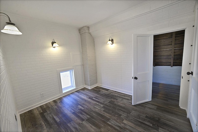 spare room featuring dark wood-type flooring and brick wall