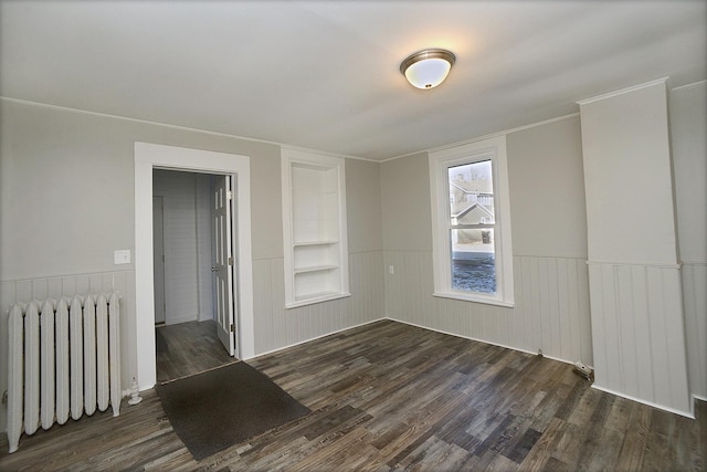 unfurnished room featuring built in shelves, dark hardwood / wood-style flooring, and radiator heating unit