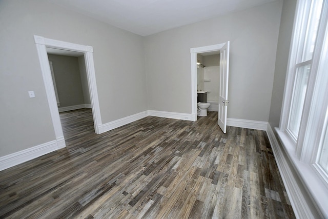 unfurnished bedroom featuring ensuite bathroom and dark hardwood / wood-style floors