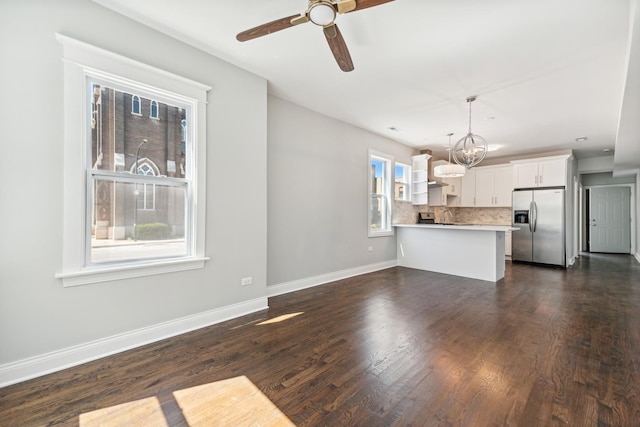 unfurnished living room with ceiling fan with notable chandelier and dark wood-type flooring