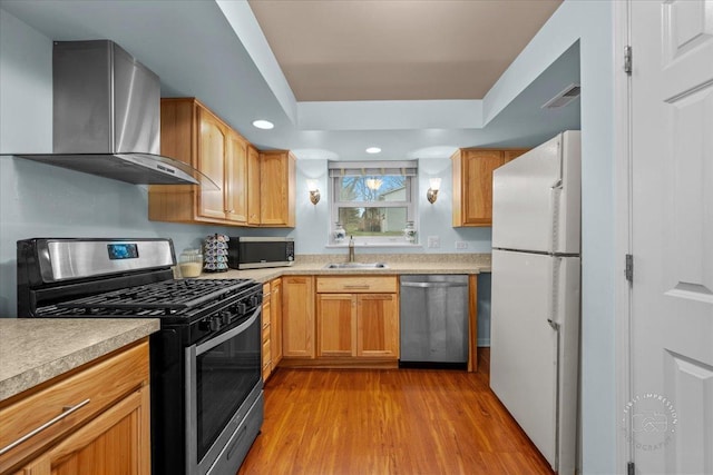 kitchen featuring sink, stainless steel appliances, light hardwood / wood-style floors, and wall chimney range hood