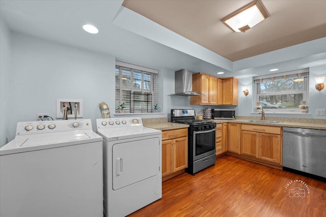 kitchen with sink, wall chimney exhaust hood, stainless steel appliances, independent washer and dryer, and light wood-type flooring