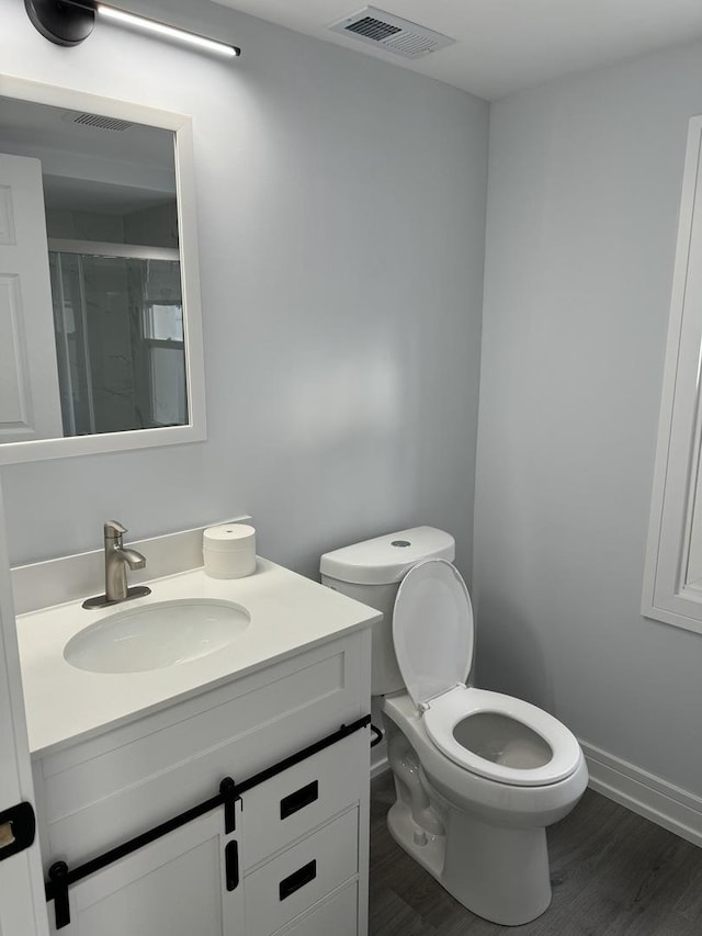 bathroom featuring vanity, hardwood / wood-style flooring, toilet, and a shower with door