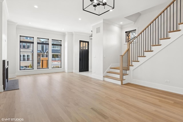 unfurnished living room with an inviting chandelier, ornamental molding, and light hardwood / wood-style floors