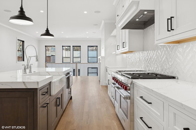 kitchen featuring custom exhaust hood, white cabinetry, decorative light fixtures, an island with sink, and stainless steel stove