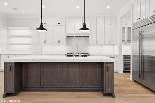 kitchen featuring built in fridge, pendant lighting, a center island with sink, and light stone counters