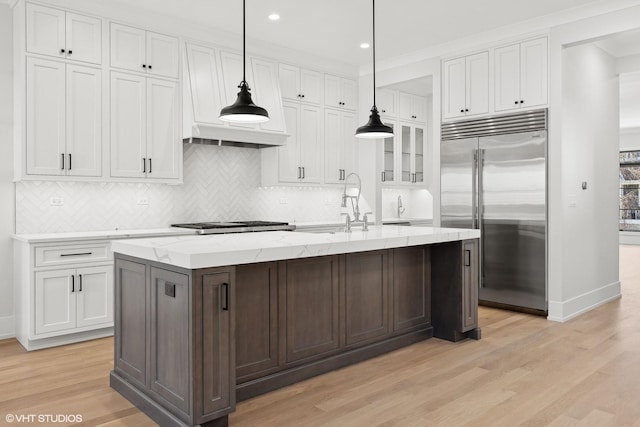 kitchen with white cabinetry, light hardwood / wood-style flooring, pendant lighting, stainless steel appliances, and a kitchen island with sink