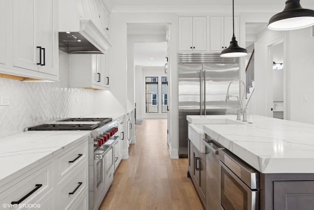 kitchen featuring white cabinetry, built in appliances, light stone countertops, and hanging light fixtures