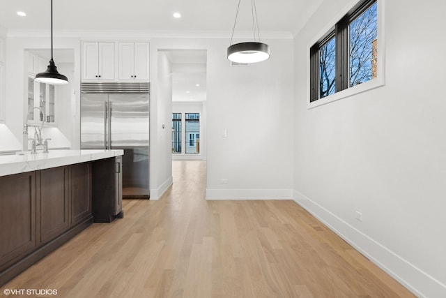 kitchen with sink, light stone counters, built in refrigerator, pendant lighting, and white cabinets