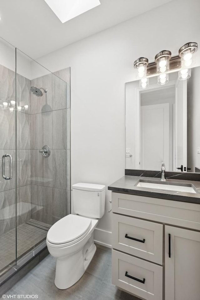 bathroom featuring vanity, a skylight, a shower with shower door, and toilet