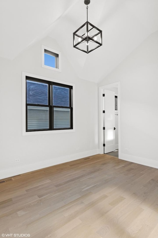 empty room with a chandelier, vaulted ceiling, and light hardwood / wood-style flooring