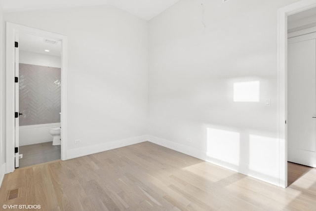 unfurnished bedroom featuring lofted ceiling, connected bathroom, and light hardwood / wood-style flooring