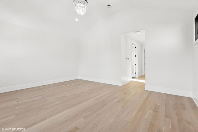 spare room featuring an inviting chandelier, lofted ceiling, and light hardwood / wood-style flooring