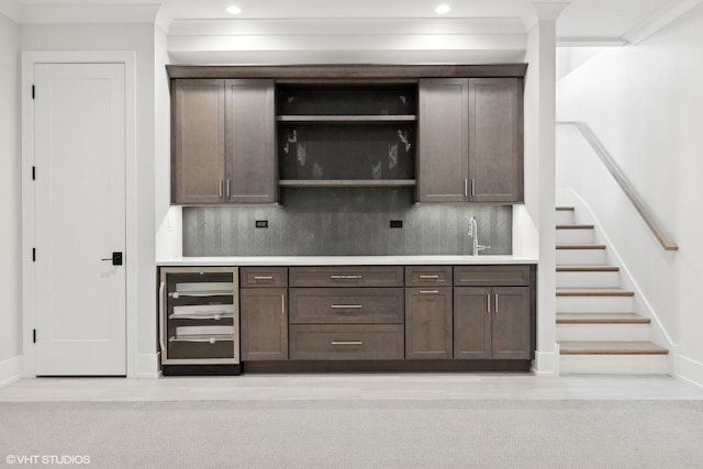 bar with dark brown cabinetry, sink, ornamental molding, beverage cooler, and backsplash