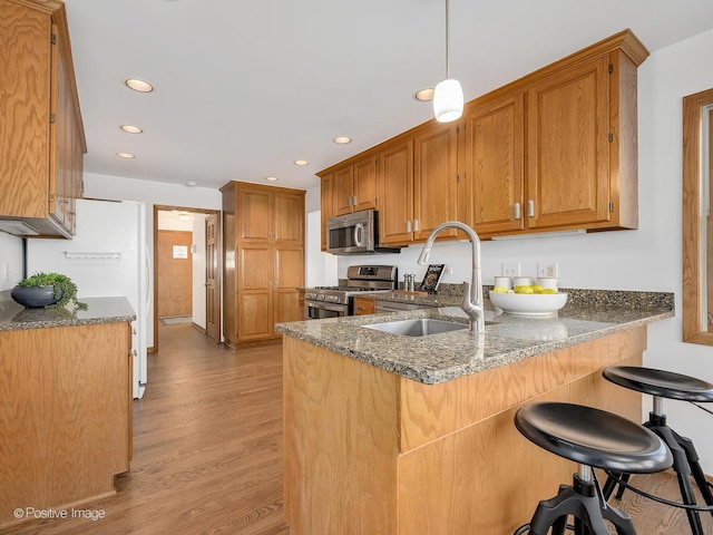 kitchen with sink, stainless steel appliances, kitchen peninsula, dark stone countertops, and light hardwood / wood-style floors