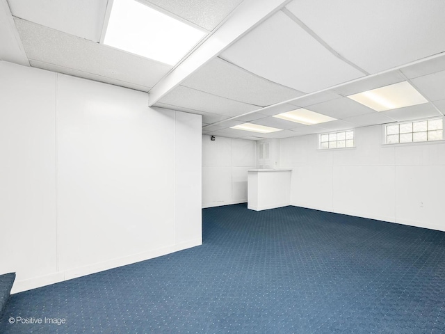 basement with a paneled ceiling and dark colored carpet