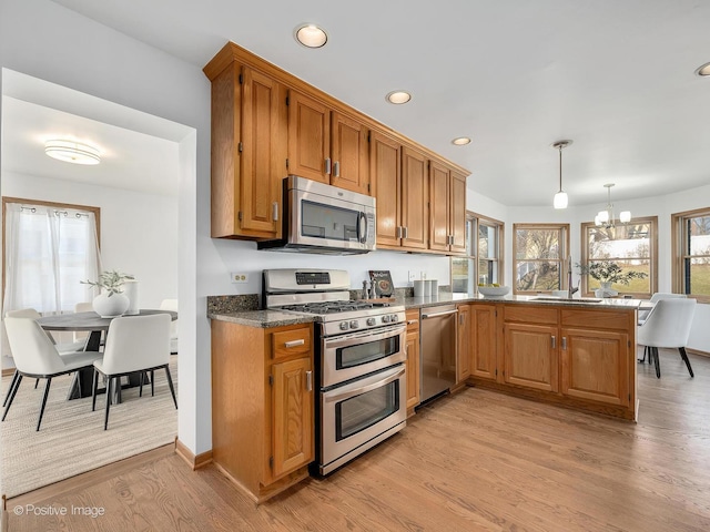 kitchen featuring sink, light hardwood / wood-style flooring, pendant lighting, a chandelier, and appliances with stainless steel finishes