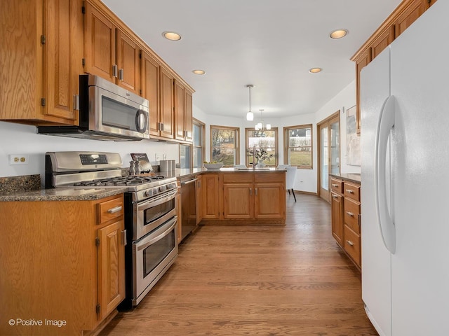 kitchen with kitchen peninsula, appliances with stainless steel finishes, pendant lighting, an inviting chandelier, and light hardwood / wood-style flooring