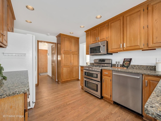 kitchen with appliances with stainless steel finishes, light wood-type flooring, and dark stone counters