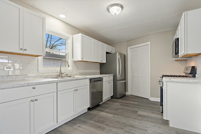 kitchen featuring appliances with stainless steel finishes, backsplash, sink, white cabinets, and light hardwood / wood-style floors