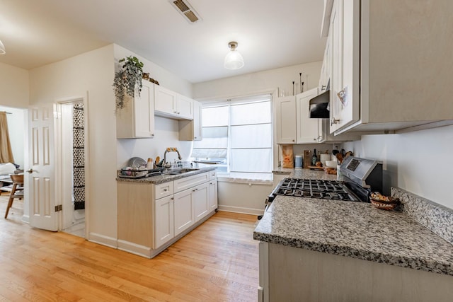 kitchen with light stone counters, white cabinetry, light wood-type flooring, and gas range