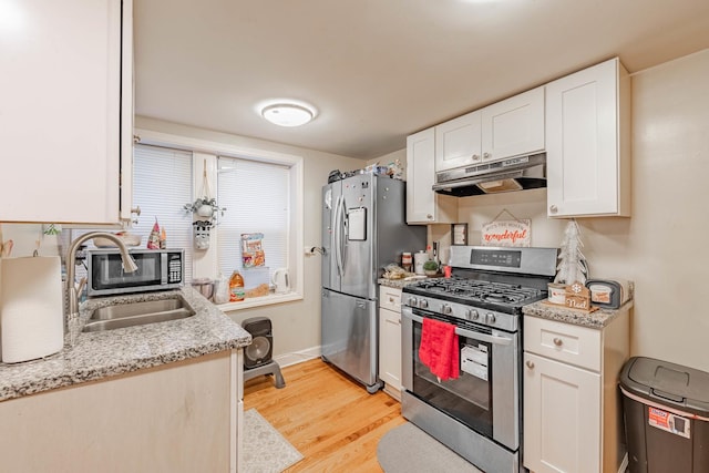 kitchen with light stone countertops, white cabinetry, sink, stainless steel appliances, and light hardwood / wood-style flooring