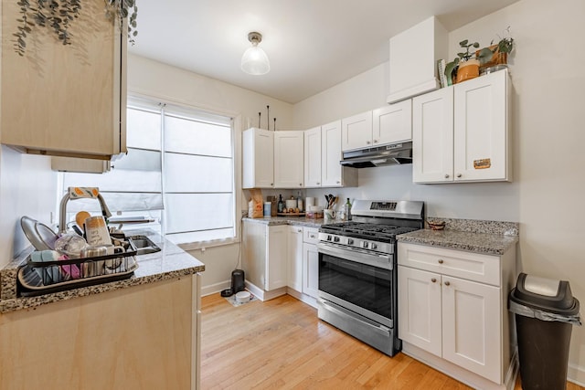 kitchen featuring white cabinets, light stone counters, light wood-type flooring, and gas range