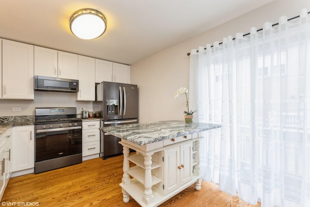 kitchen with white cabinetry, stainless steel appliances, light stone counters, and light wood-type flooring