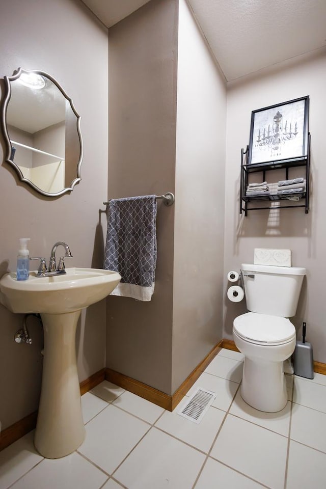 half bathroom featuring visible vents, toilet, a sink, baseboards, and tile patterned floors