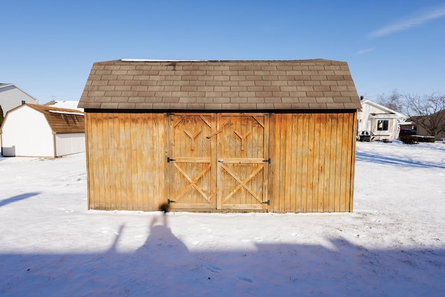 snow covered structure featuring an outbuilding and a storage unit