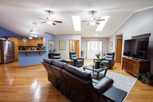 living room featuring vaulted ceiling with skylight, ceiling fan, and light wood finished floors