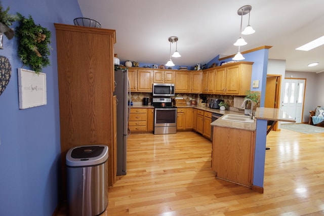 kitchen featuring sink, backsplash, kitchen peninsula, decorative light fixtures, and appliances with stainless steel finishes