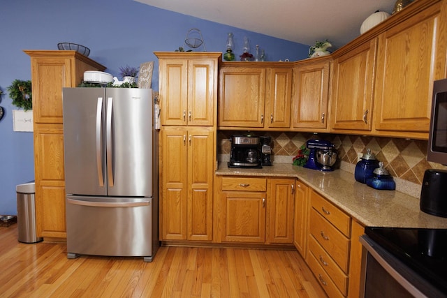 kitchen with light stone countertops, light wood-type flooring, tasteful backsplash, stainless steel appliances, and lofted ceiling