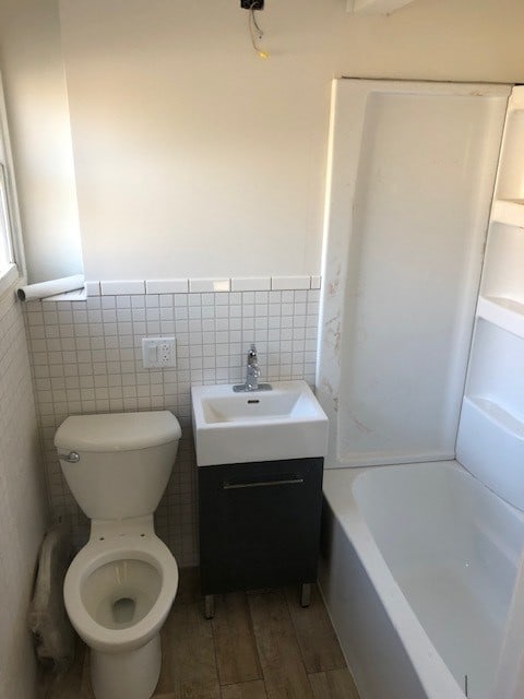 bathroom featuring hardwood / wood-style flooring, tile walls, toilet, and vanity