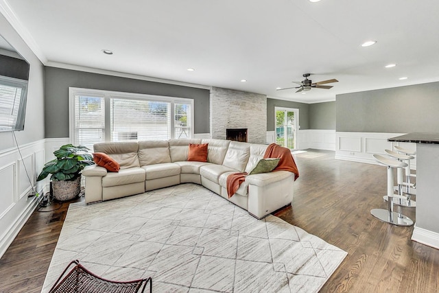 living room with a stone fireplace, hardwood / wood-style flooring, ceiling fan, and ornamental molding