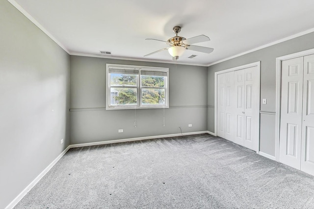 unfurnished bedroom with carpet flooring, ceiling fan, ornamental molding, and two closets