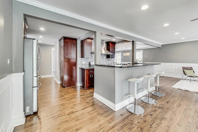 kitchen with backsplash, crown molding, wall chimney exhaust hood, stainless steel fridge, and light hardwood / wood-style floors