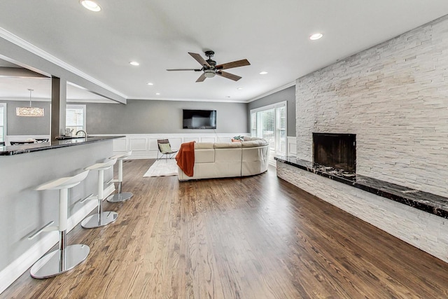 unfurnished living room featuring ceiling fan, a stone fireplace, ornamental molding, and wood-type flooring