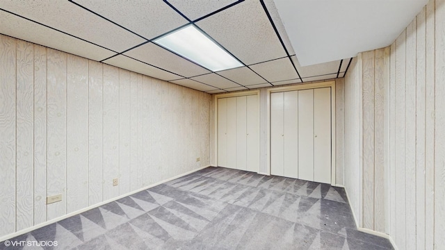 unfurnished bedroom featuring a paneled ceiling, wood walls, and carpet floors