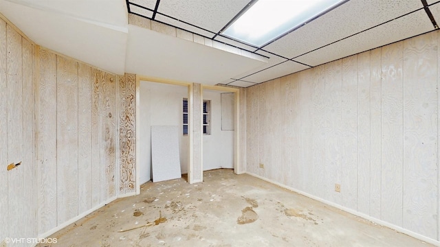 empty room with a paneled ceiling, wood walls, and concrete floors