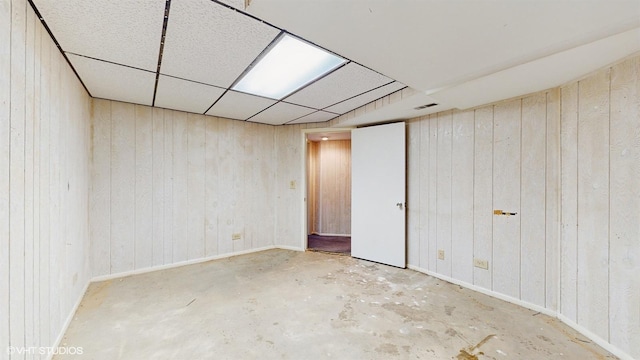 basement featuring a drop ceiling and wooden walls