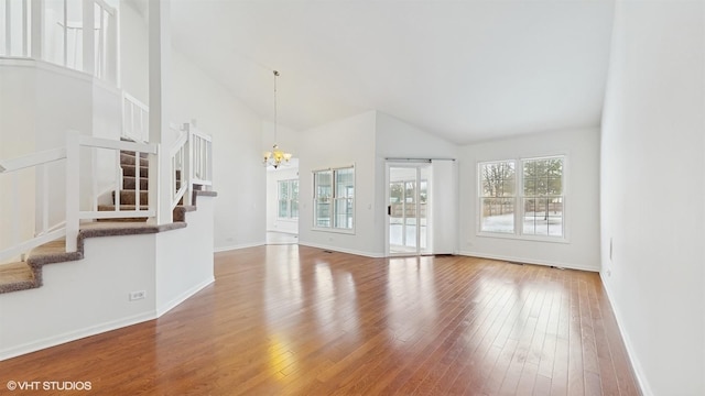 unfurnished living room featuring hardwood / wood-style floors, a notable chandelier, and high vaulted ceiling