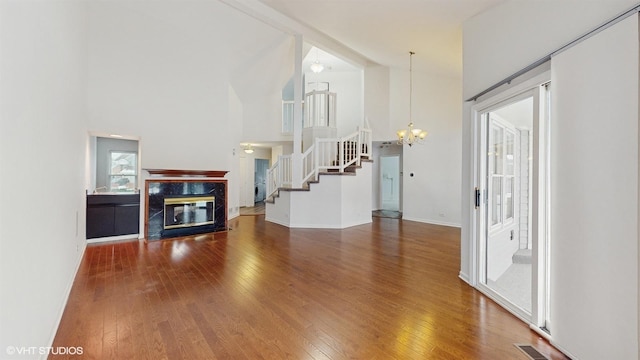 unfurnished living room with a high end fireplace, wood-type flooring, an inviting chandelier, and a high ceiling