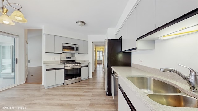 kitchen with appliances with stainless steel finishes, light hardwood / wood-style floors, hanging light fixtures, and sink